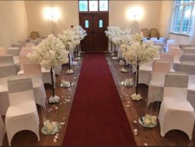 dressed wedding ceremony picture with chairs covered in white, fake petal blossom trees and a red aisle carpet