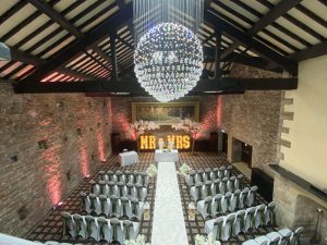 Wedding ceremony venue dresses with chairs in white covers and sage sashes with Mrs and Mrs light up letters and glitterball