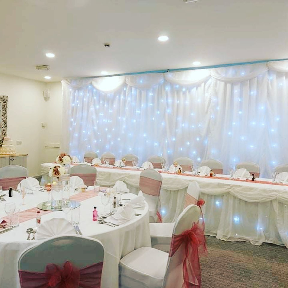 Wedding venue dressed with white material swags, starlight backdrop and chair covers and sashes.