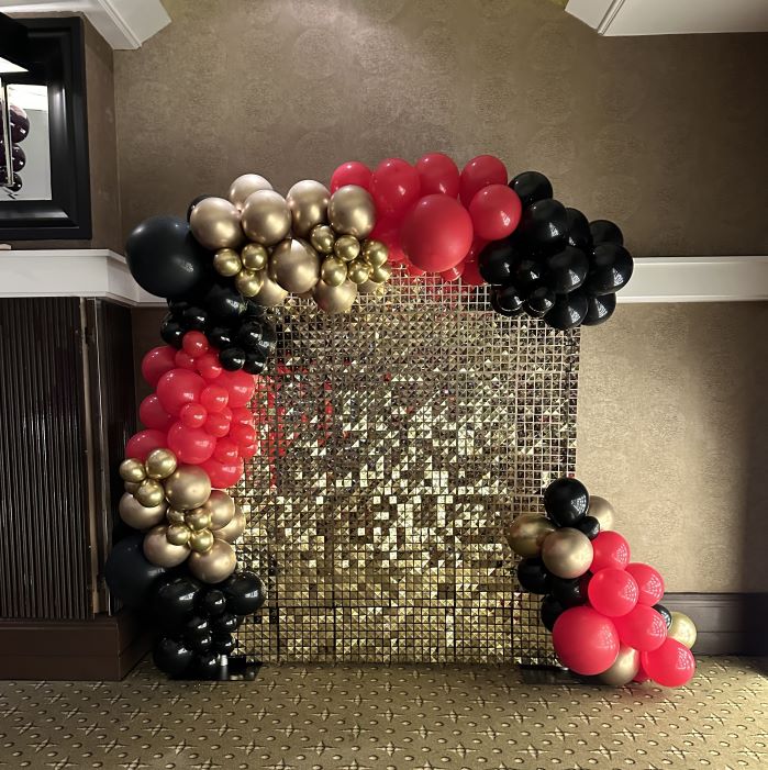 gold glitter wall for party or event dressed with gold, red and black balloon garland
